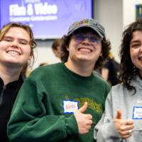 Three students smiling and giving thumbs up to the camera